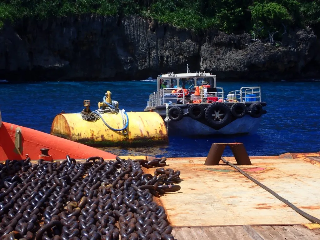 a small boat anchored in a small cove next to a large set of chains on the dock