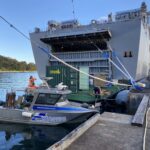 small Franmarine work boat next to a large naval ship wih Franmarine workers on board