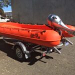 A small orange rubber duck boat on a pulling trailer