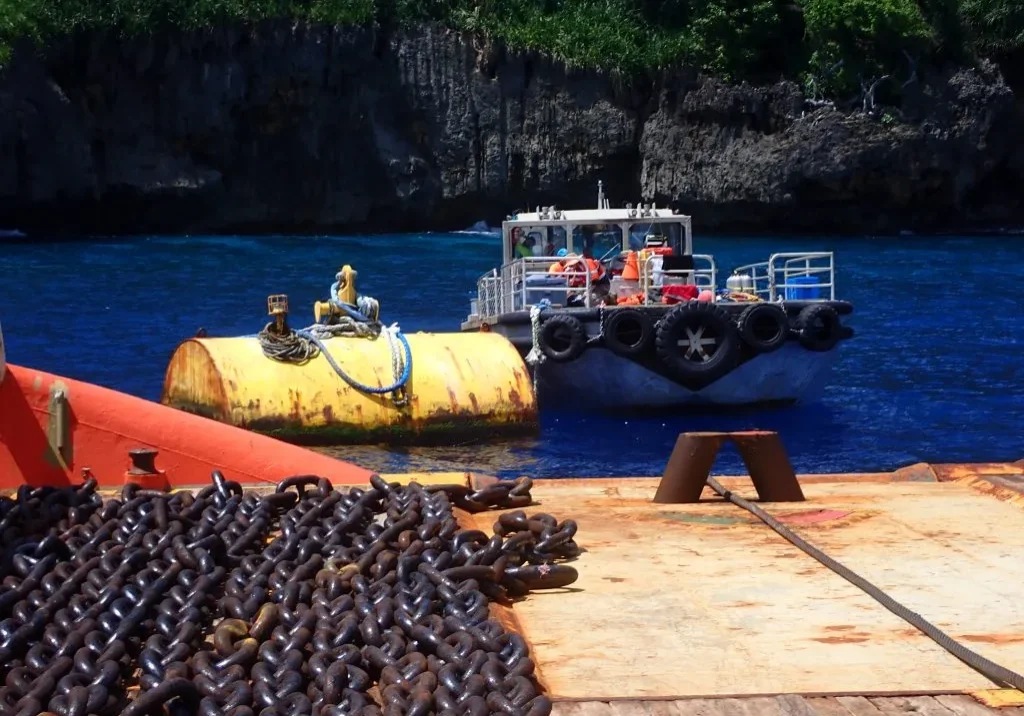 a small boat anchored in a small cove next to a large set of chains on the dock